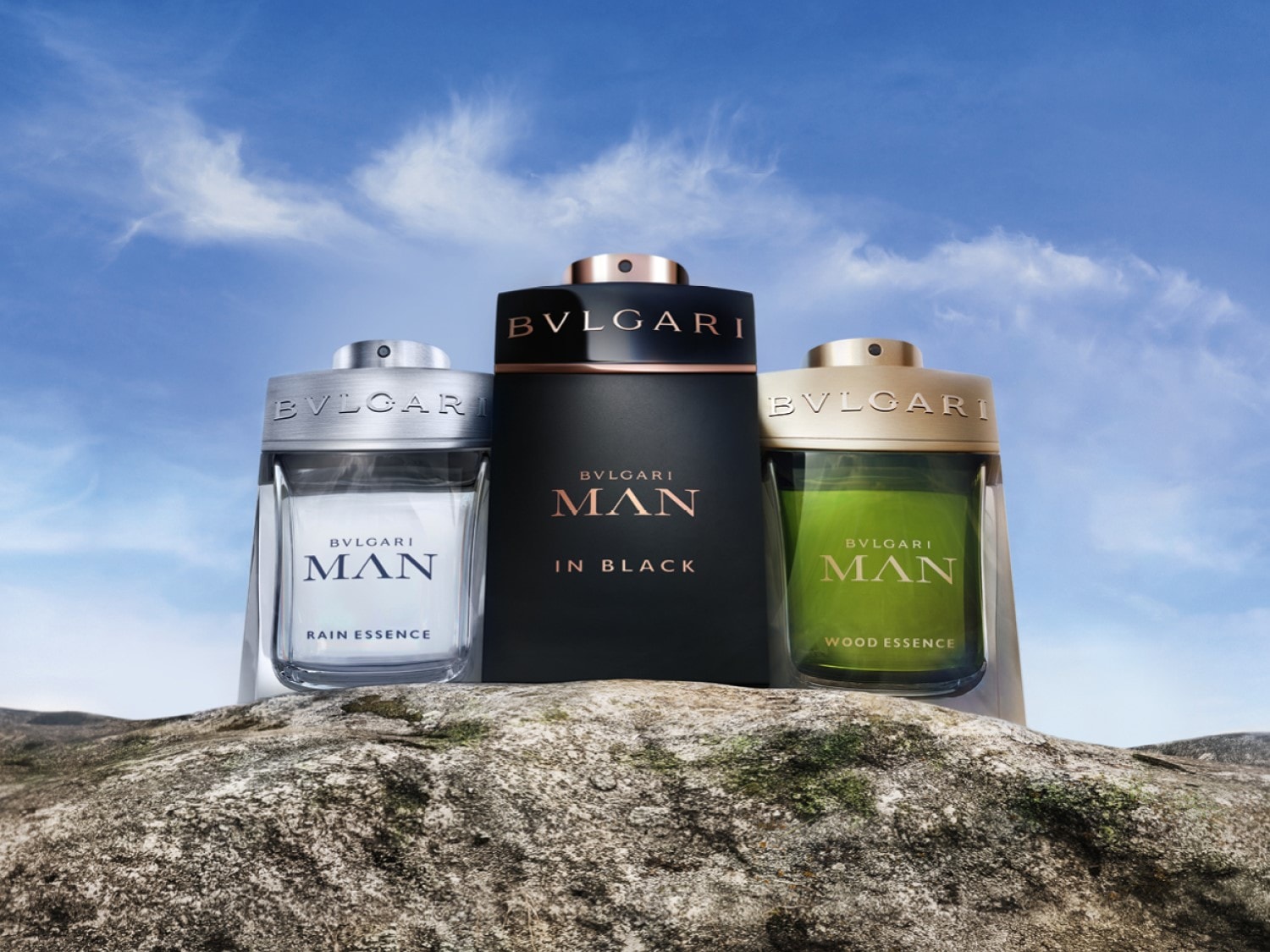 Drei Bulgari MAN Düfte stehen auf einem Felsen vor einem Himmel: Rain Essence, In Black und Wood Essence.