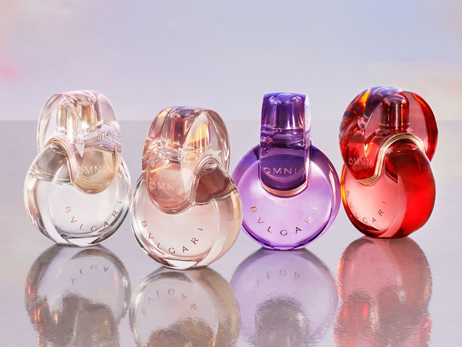 Nahaufnahme von vier Bvlgari Omnia Parfümflaschen in verschiedenen Farben: klar, rosa, lila und rot, die auf einer reflektierenden Oberfläche stehen.
