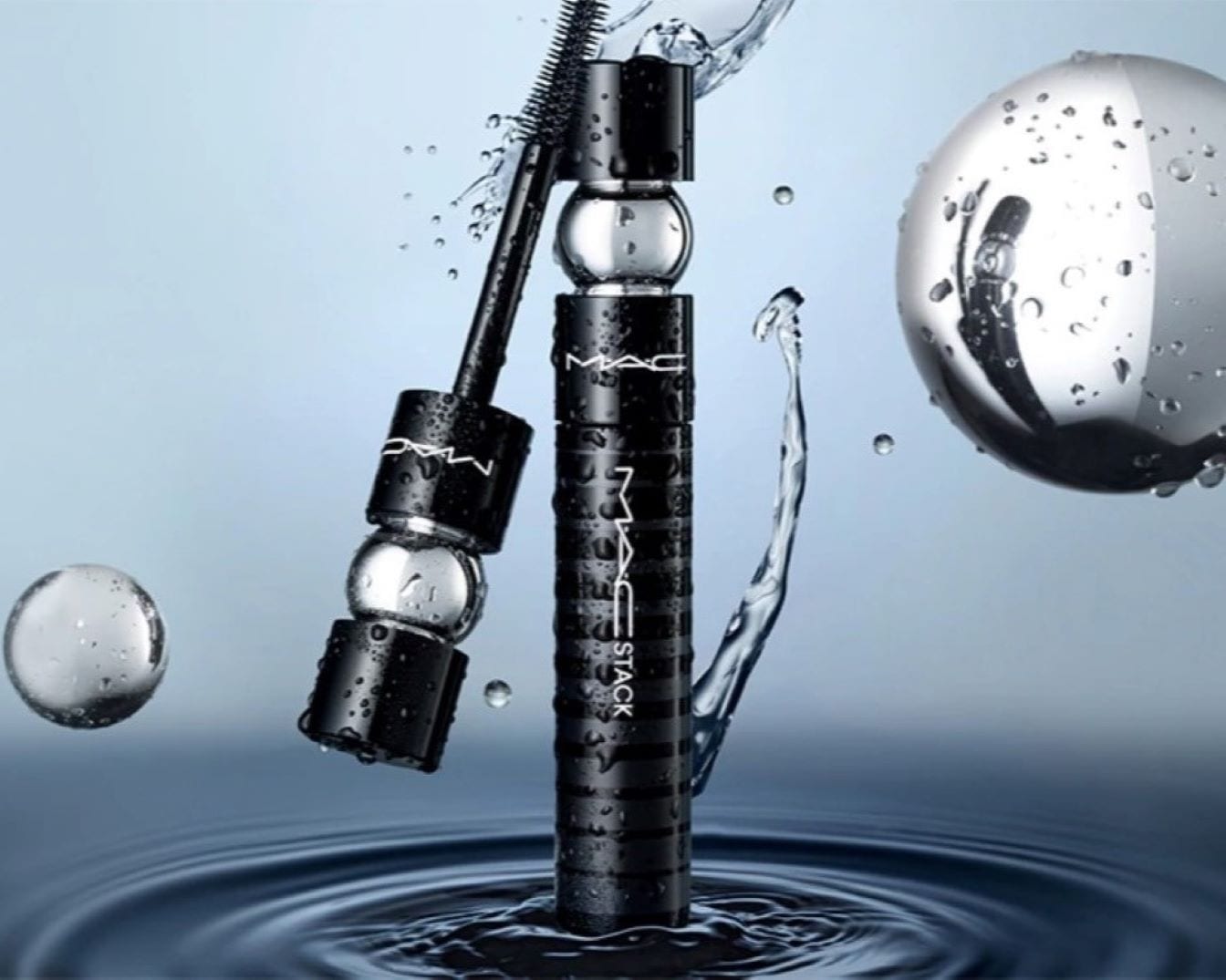 Die schwarze MAC Stack Mascara präsentiert sich in einer dynamischen Szene mit Wassertropfen und -spritzern.