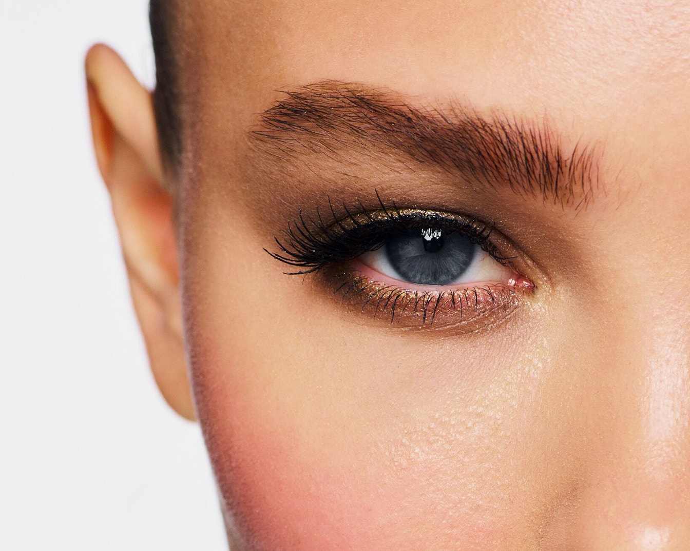 Close-up van een blauw oog met bruine oogschaduw en lange zwarte wimpers, de huid heeft een zachte roze blos.