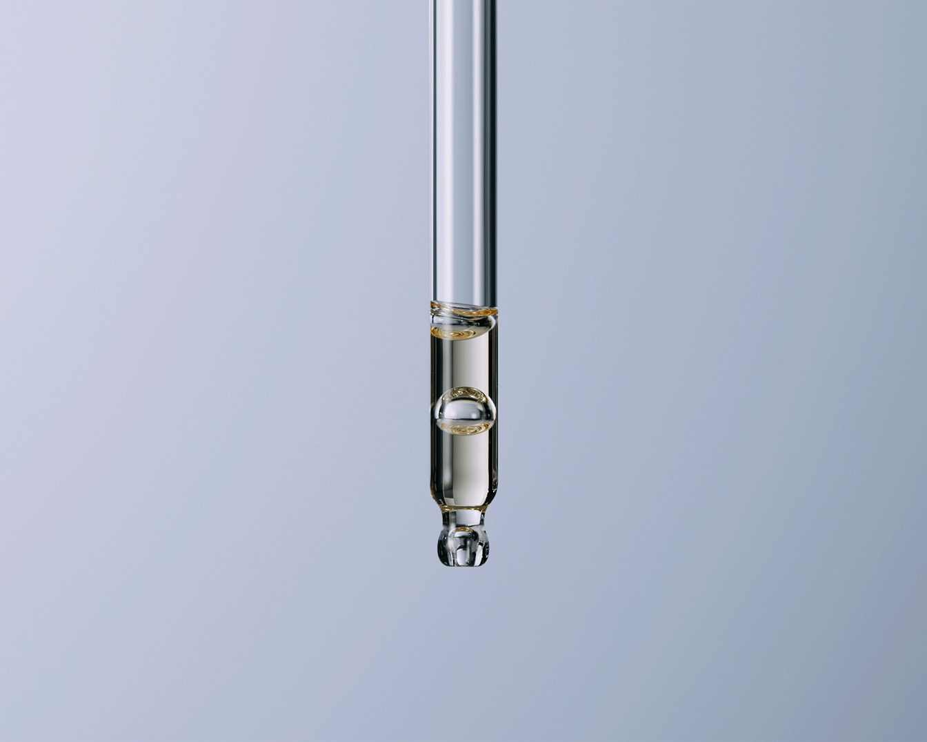 Primo piano di un contagocce in vetro trasparente riempito con un liquido dorato e limpido, che mostra bolle d'aria all'interno, su uno sfondo blu tenue.