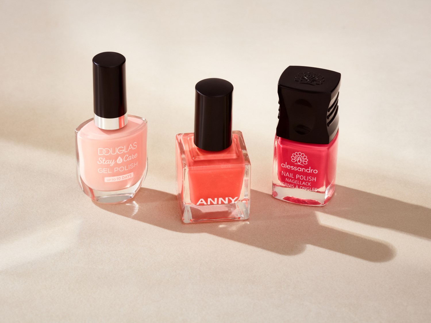 Drie nagellakken van Douglas Stay & Care Gel Polish in een zachte perzikkleur, Anny in een heldere koraaltint en Alessandro Nail Polish in een levendige roze tint.