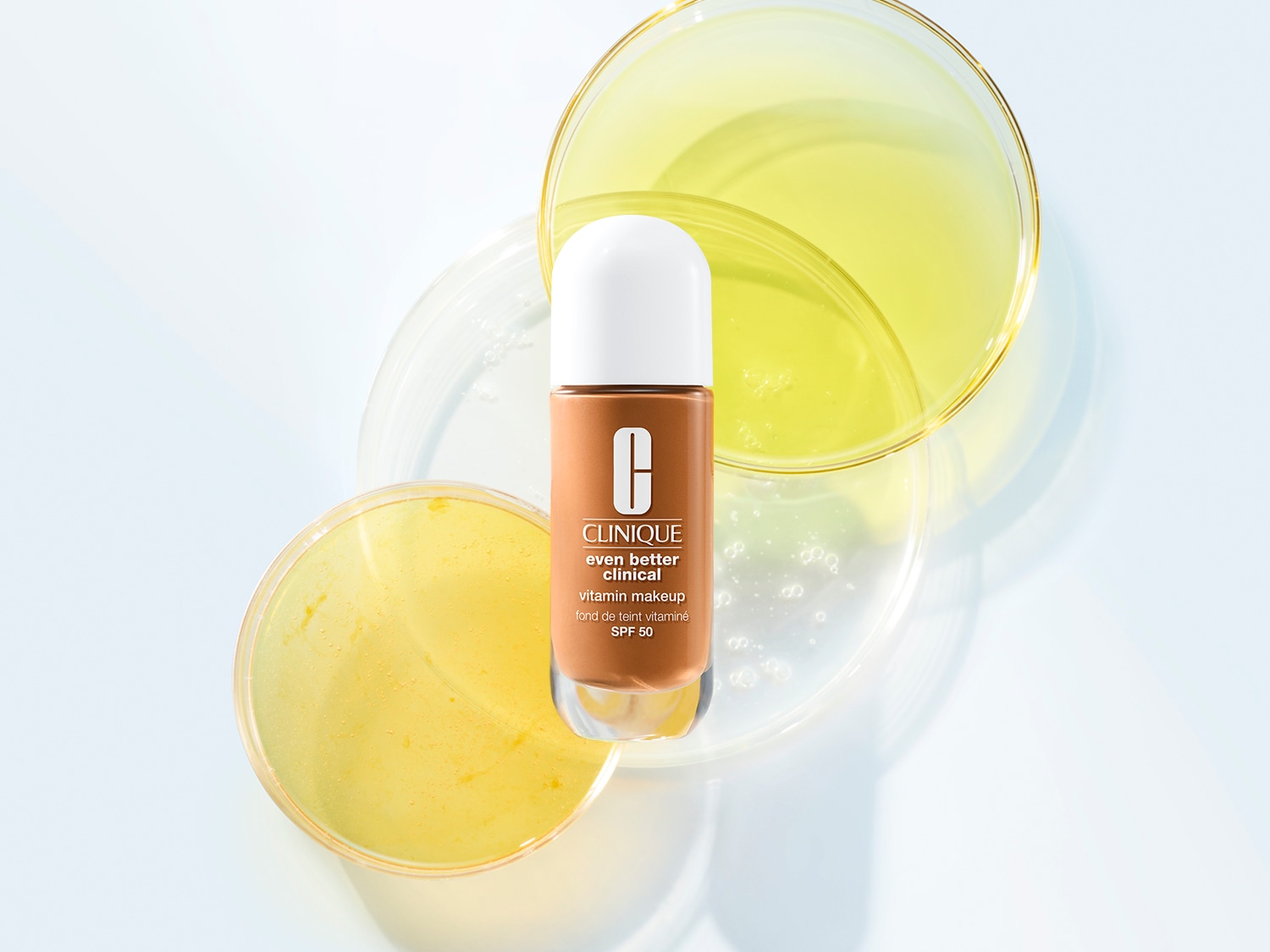 Clinique Even Better Clinical Vitamin Makeup SPF 50 w brązowej butelce z białym aplikatorem na tle przezroczystych szalek Petriego.