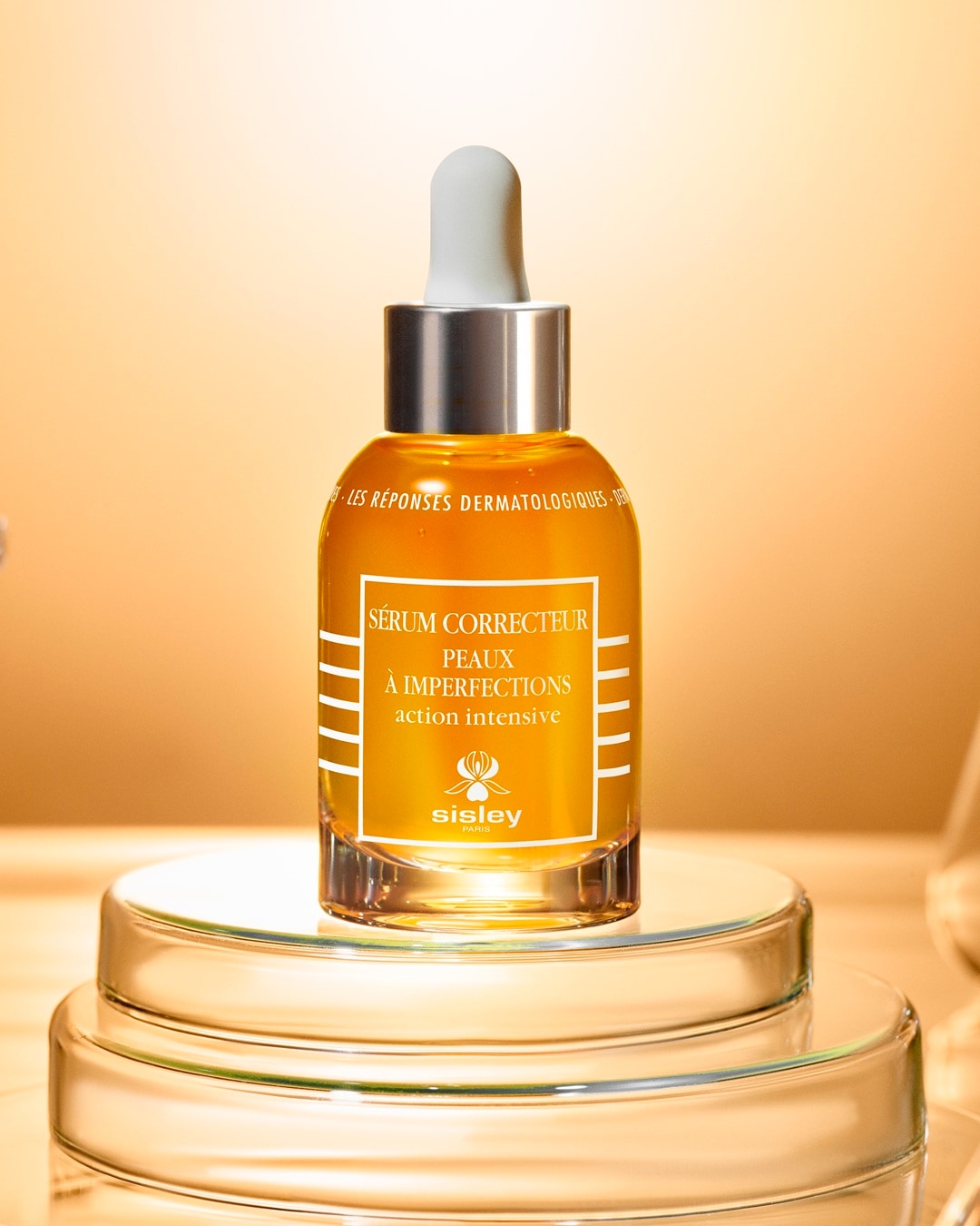 Serum korygujące Sisley Sérum Correcteur Peaux à Imperfections o intensywnym działaniu, w bursztynowej butelce z pipetą, stoi na szklanym postumencie, obiecując redukcję niedoskonałości.