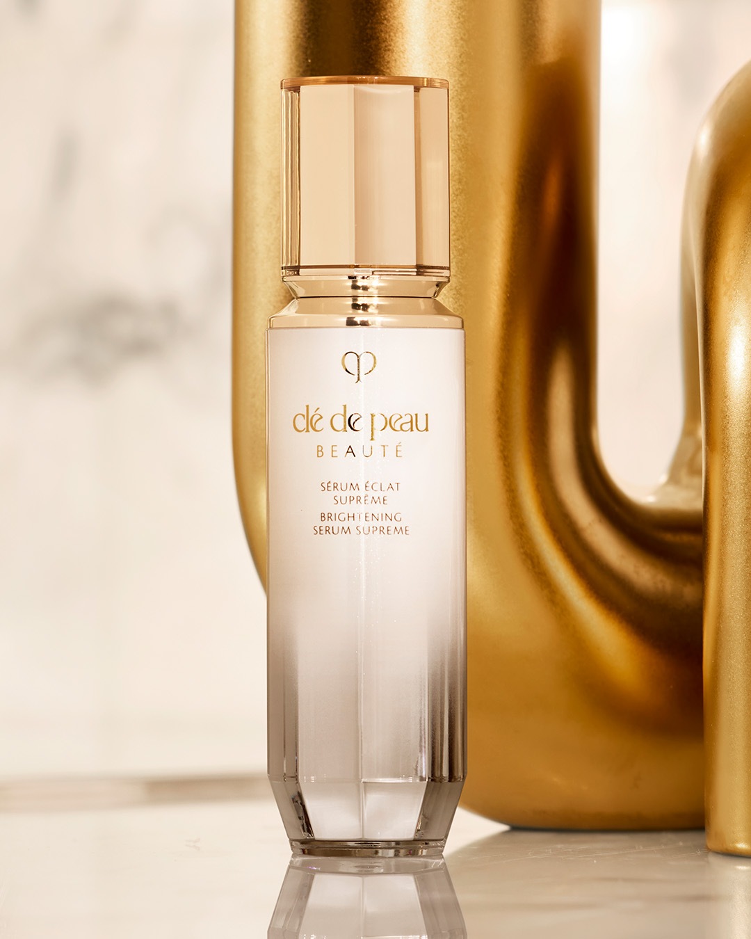 Das Clé de Peau Beauté Sérum Éclat Suprême, ein luxuriöses, weißes Serum in einer eleganten Flasche mit goldenem Verschluss, verspricht strahlende Haut.