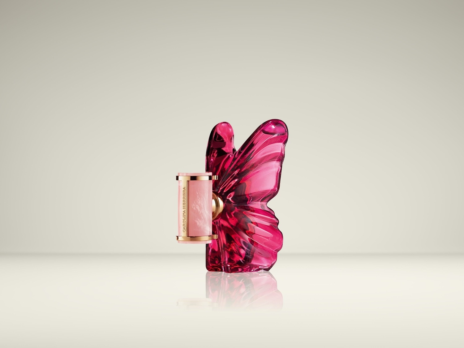 Een roze, marmeren lippenstiftkoker met gouden accenten staat naast een glanzende, doorschijnende roze vlinderfles, beide reflecterend op een licht oppervlak.