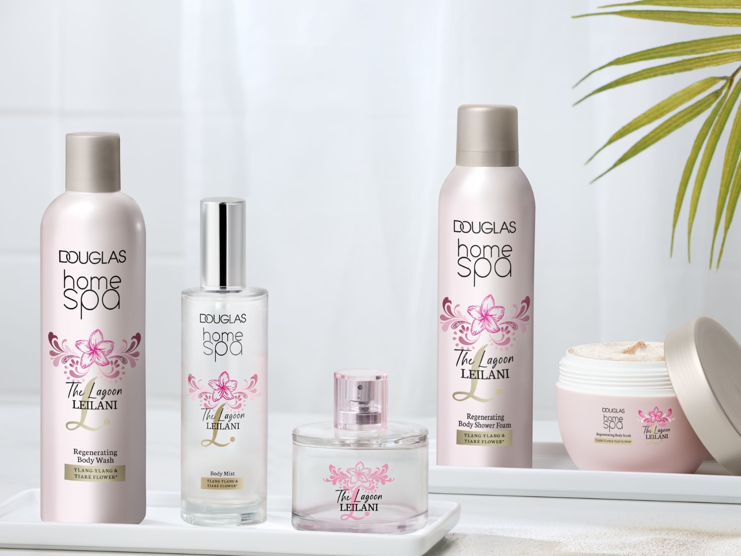 Kolekcja Douglas Home Spa The Lagoon Leilani, zawierająca regenerujący płyn do mycia ciała, mgiełkę do ciała, piankę pod prysznic i peeling do ciała, wszystkie o zapachu ylang-ylang i kwiatu tiare, jest prezentowana na białej tacy.