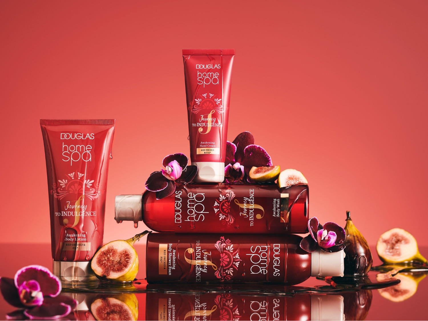 Krem do rąk Douglas Home Spa Journey to Indulgence Awakening Hand Cream z czerwoną orchideą i figą, w czerwonej tubce z białym wieczkiem, stoi na tle innych produktów z tej samej linii, otoczony orchideami i figami.