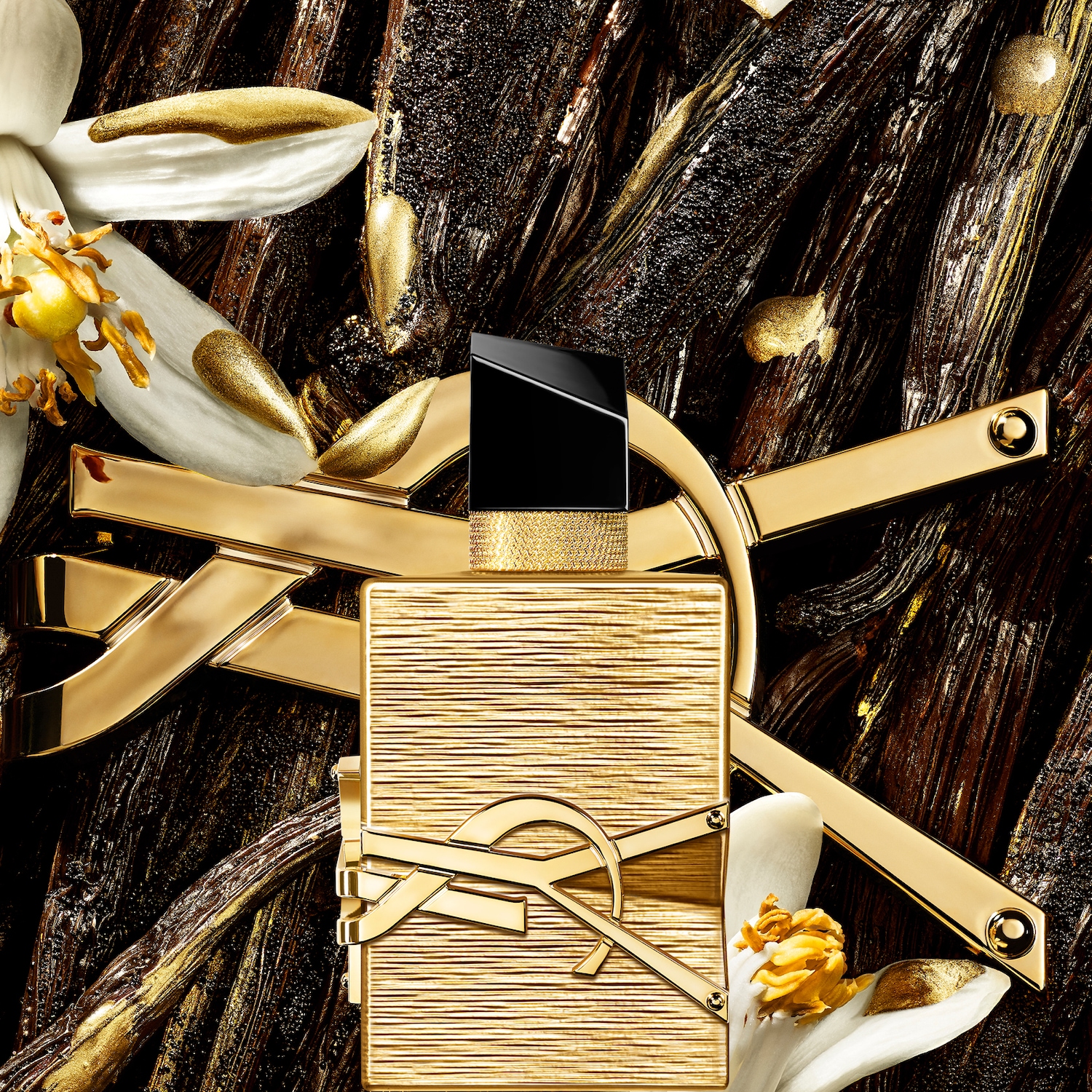Een gouden parfumflesje van Yves Saint Laurent, omringd door vanillebloemen en -peulen, ligt op een donkere ondergrond met gouden accenten.