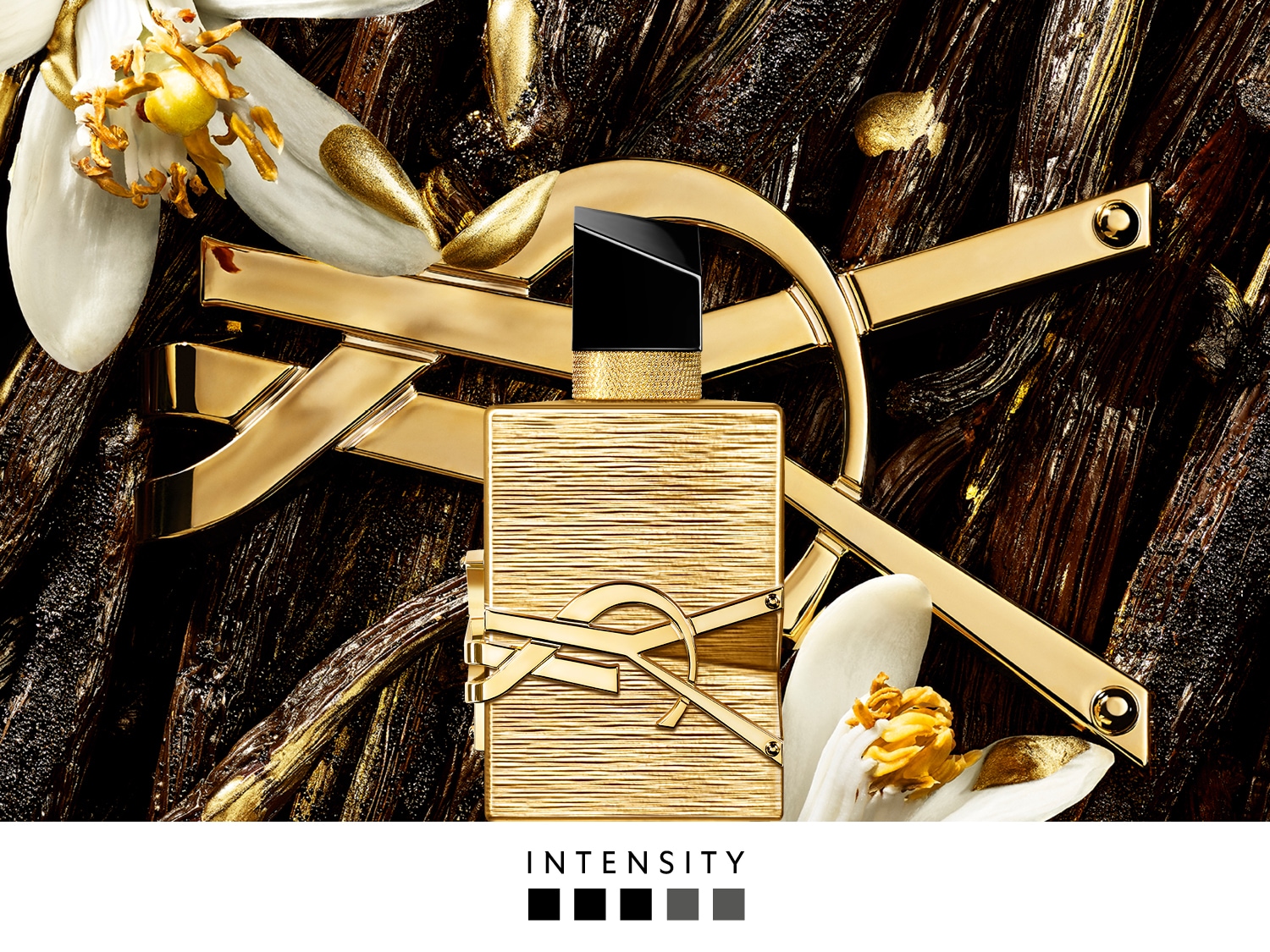 Een gouden parfumflesje met een zwart dopje en het YSL-logo, omringd door witte bloemen en gouden accenten op een donkere, houtachtige achtergrond, met het woord "INTENSITY" eronder.