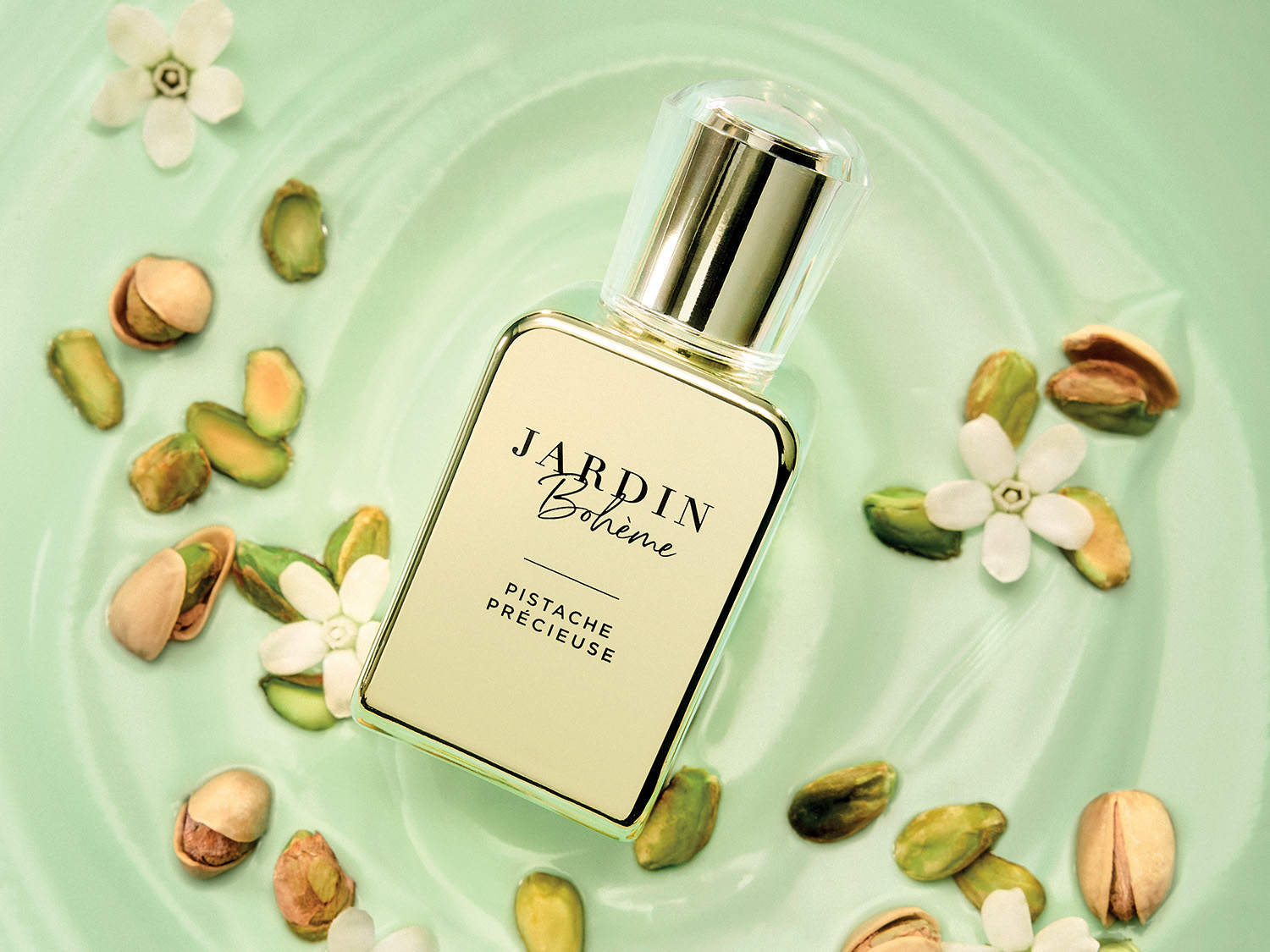 Le parfum Jardin Bohème Pistache Précieuse est présenté dans un flacon rectangulaire avec un bouchon doré et transparent, posé sur un fond vert clair orné de pistaches et de petites fleurs blanches.