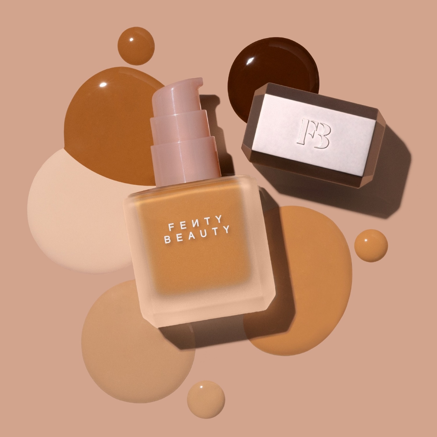 Een Fenty Beauty foundationflesje met een lichtroze pompje staat rechtop, omringd door druppels vloeibare foundation in verschillende huidtinten, van lichtbeige tot donkerbruin, en een rechthoekig doosje met het Fenty Beauty-logo.