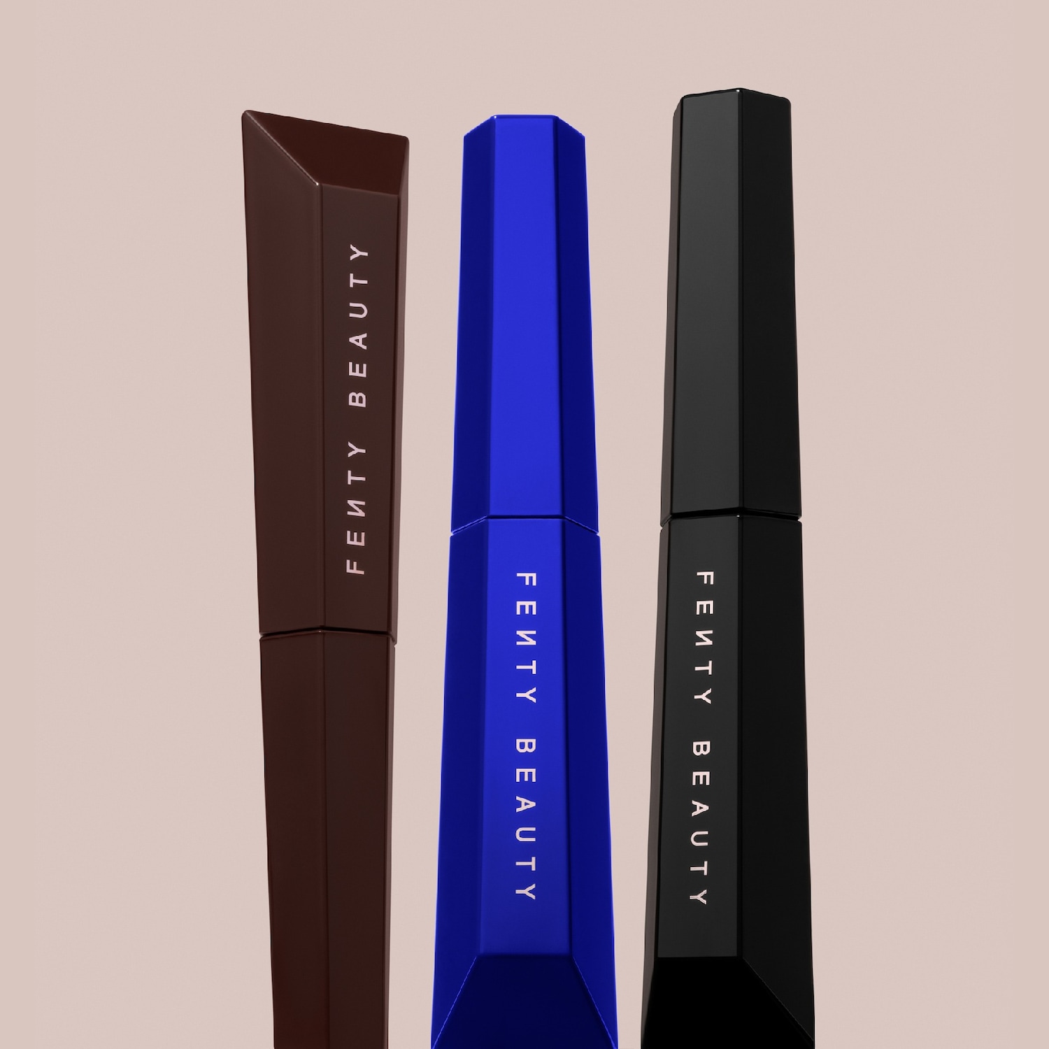 Drie Fenty Beauty mascara's in bruin, blauw en zwart, elk met het merklogo verticaal op de verpakking, staan rechtop tegen een effen achtergrond.