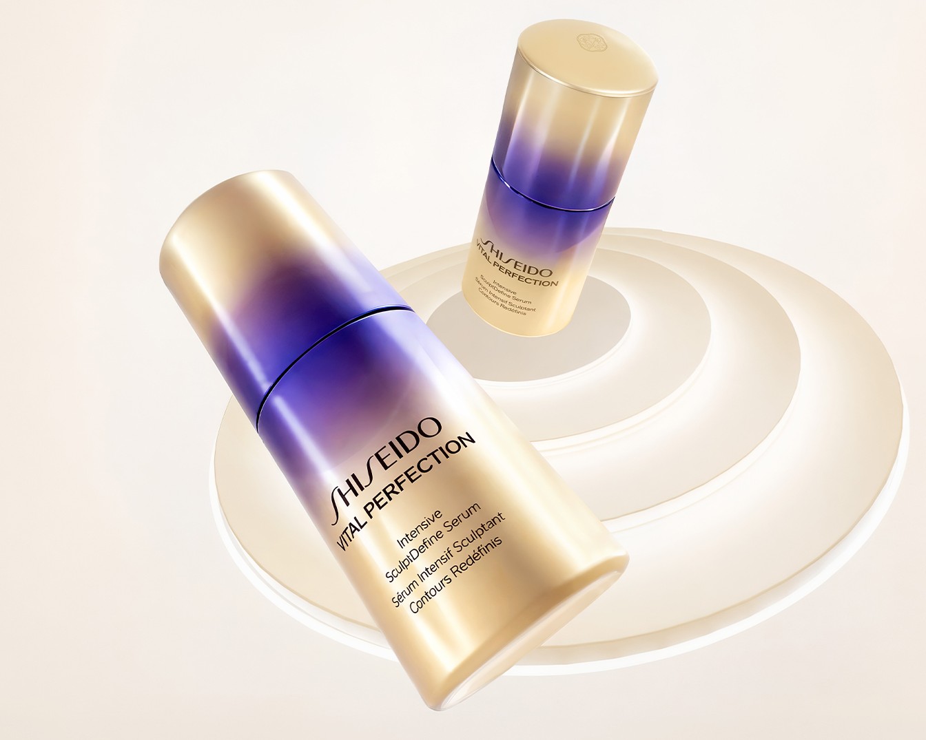 Due flaconi di siero Shiseido Vital Perfection Intensive SculptDefine, con un design elegante che sfuma dal viola all'oro, sono posizionati su una base bianca a cerchi concentrici.