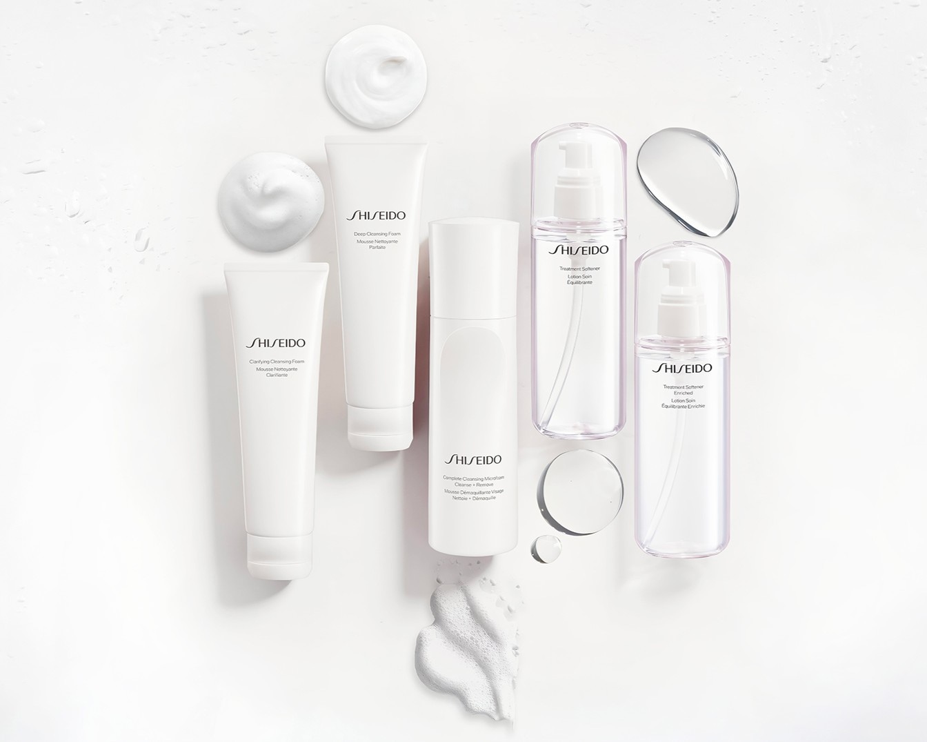 Una collezione di prodotti Shiseido, tra cui schiume detergenti e lozioni ammorbidenti, disposti su uno sfondo bianco con schiuma e goccioline d'acqua, che mostrano la loro texture e il loro packaging elegante.