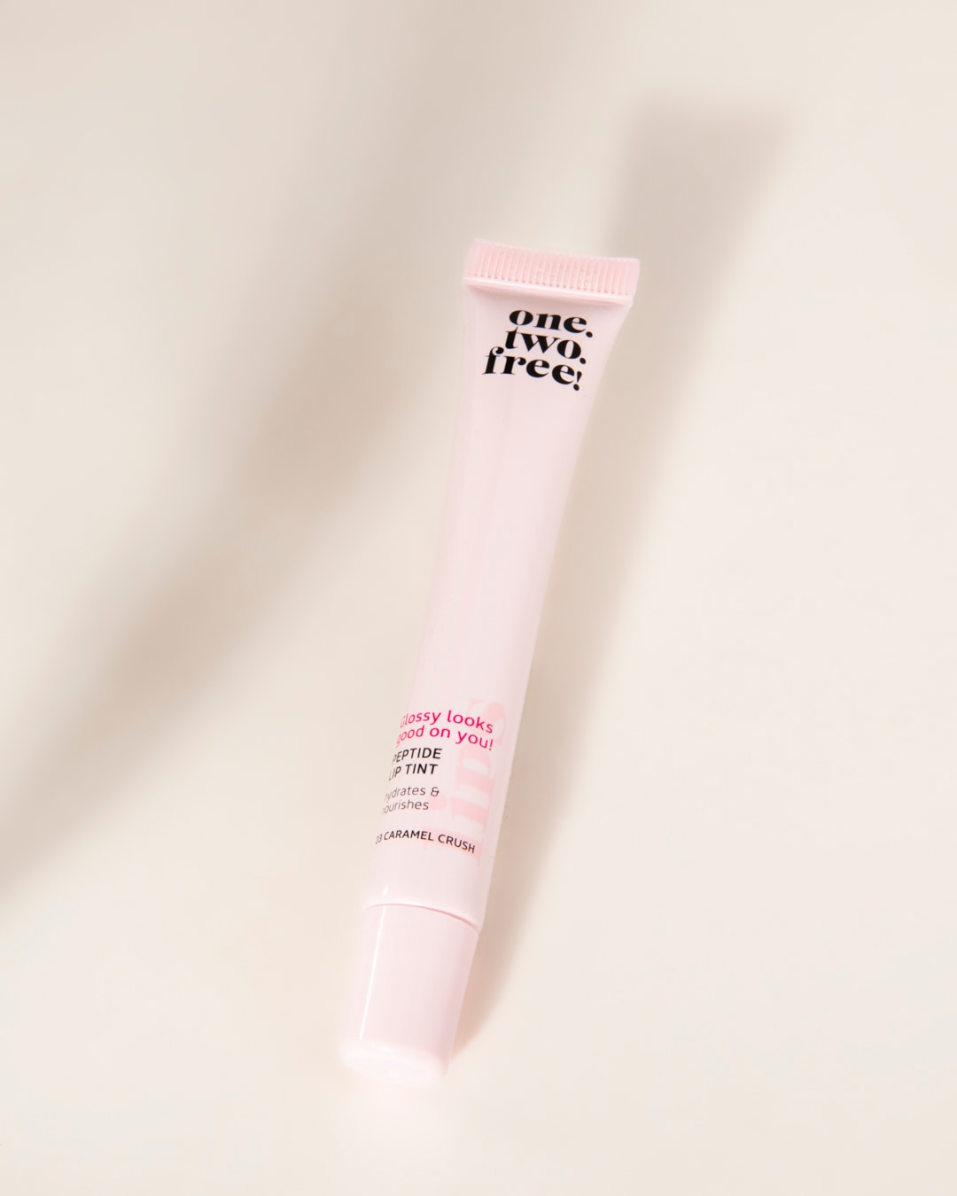 Le brillant à lèvres One.Two.Free! Peptide Lip Tint en teinte Caramel Crush, présenté dans un tube rose pâle, hydrate et nourrit les lèvres pour un fini glossy.