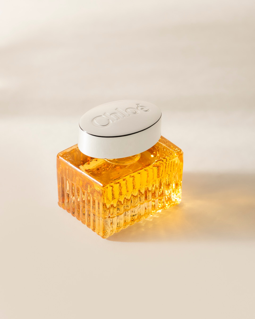 Le parfum Chloé, présenté dans un flacon en verre texturé de couleur ambre avec un bouchon blanc ovale orné du logo Chloé en relief, évoque une élégance intemporelle.