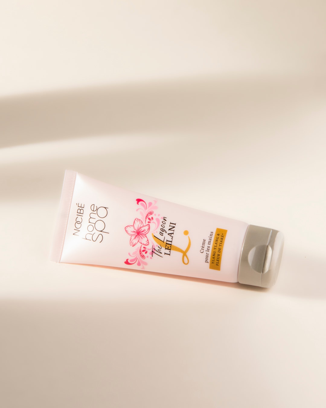 La crème pour les mains Nocibé Home Spa The Lagoon Leilani, présentée dans un tube rose pâle avec des motifs floraux, est enrichie en Ylang-Ylang et Fleur de Tiaré pour une hydratation douce et parfumée.