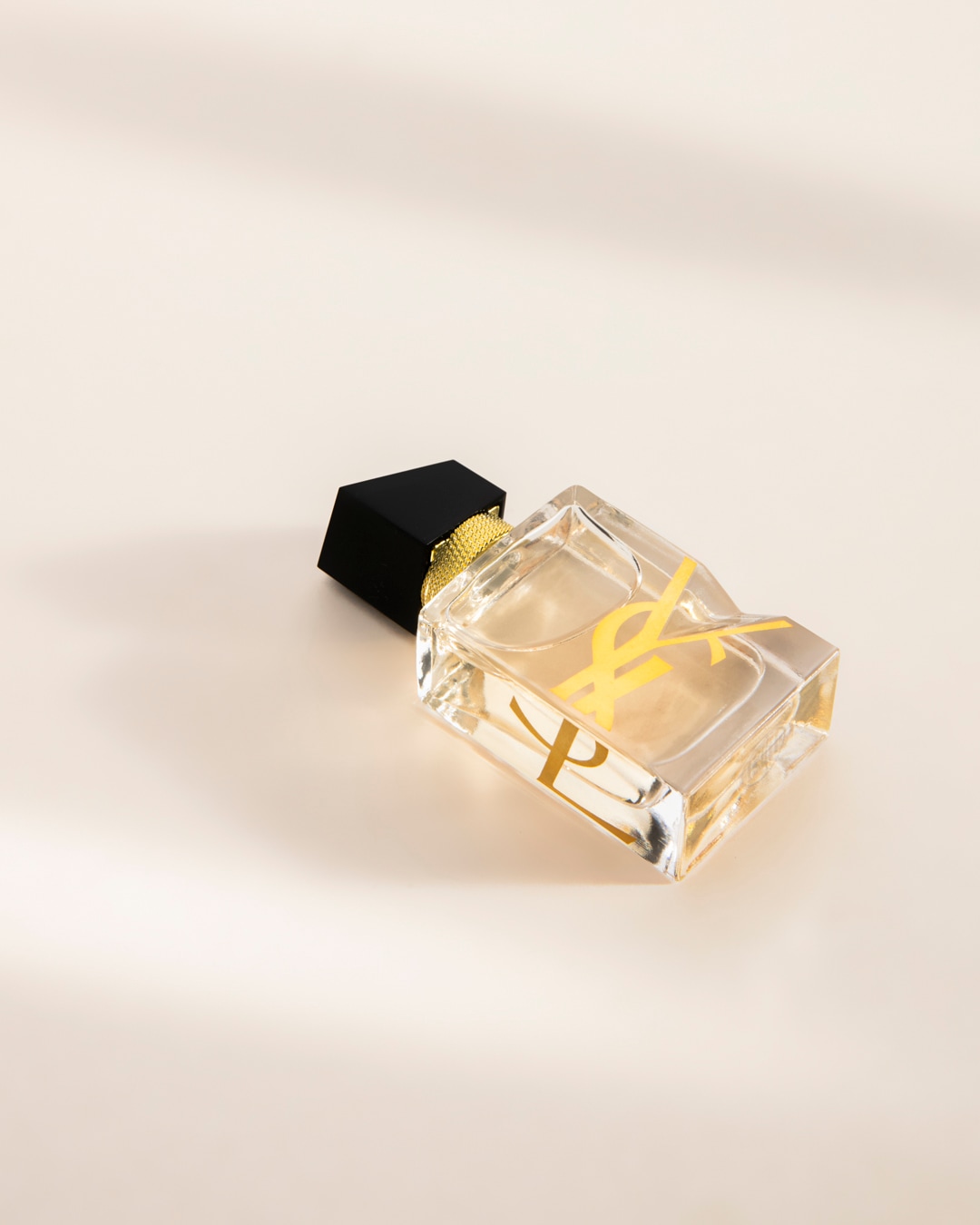 Le parfum Libre d'Yves Saint Laurent est présenté dans un flacon rectangulaire en verre transparent avec un liquide ambré, orné du logo YSL doré et d'un bouchon noir et or.