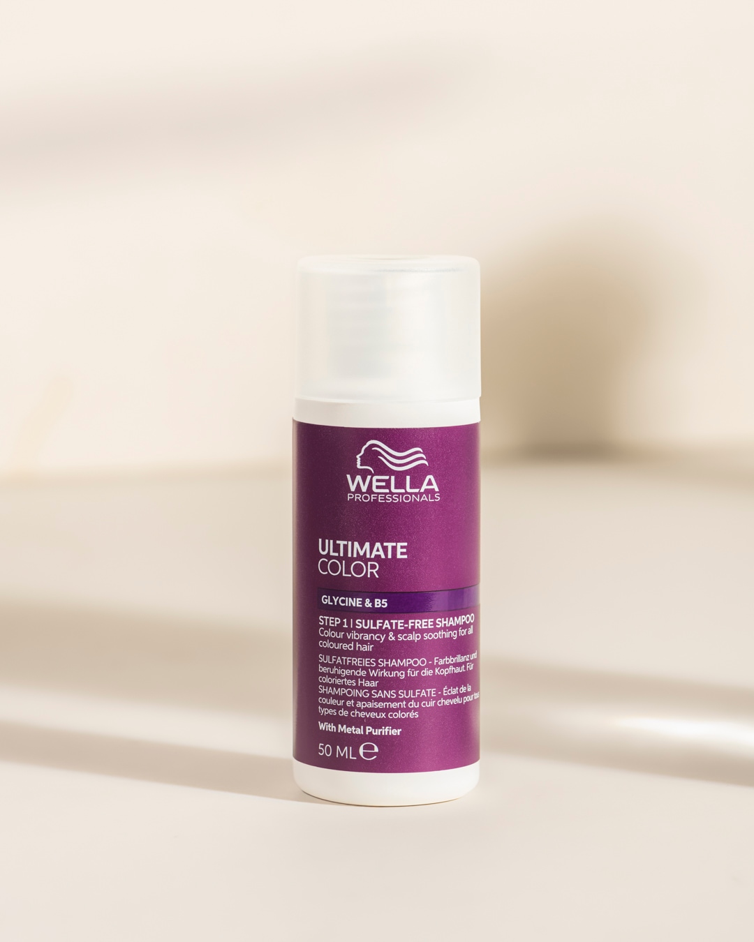 Le shampooing sans sulfate Wella Professionals Ultimate Color de 50 ml, dans un flacon violet et blanc, est formulé avec de la glycine et de la vitamine B5 pour raviver la couleur et apaiser le cuir chevelu des cheveux colorés.