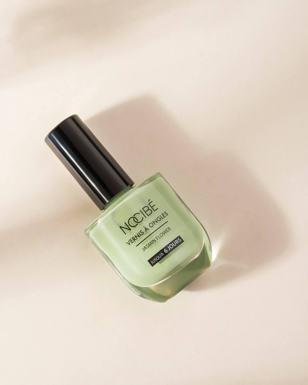 Le vernis à ongles Nocibé Jasmin Flower, d'une teinte vert clair, est présenté dans un flacon en verre transparent avec un bouchon noir, promettant une tenue jusqu'à 6 jours.