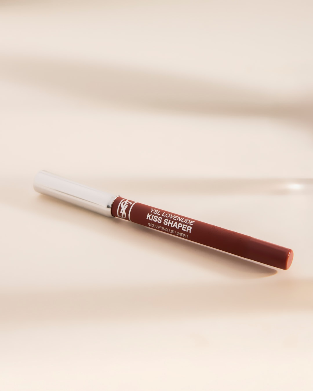 Le crayon à lèvres YSL Lovenude Kiss Shaper, de couleur marron, est doté d'un capuchon argenté et d'un corps marron avec le logo YSL, idéal pour sculpter et définir vos lèvres.