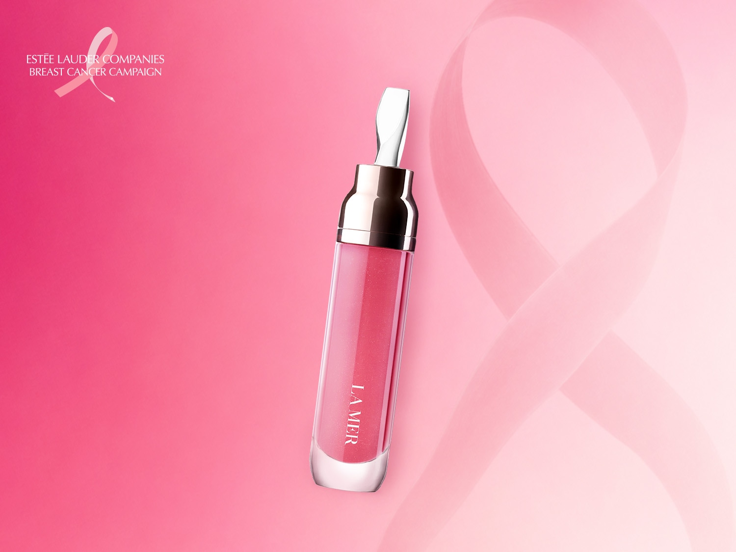 Błyszczyk do ust La Mer w odcieniu różowym, z aplikatorem, na tle różowej wstążki symbolizującej kampanię Estée Lauder Companies Breast Cancer Campaign.