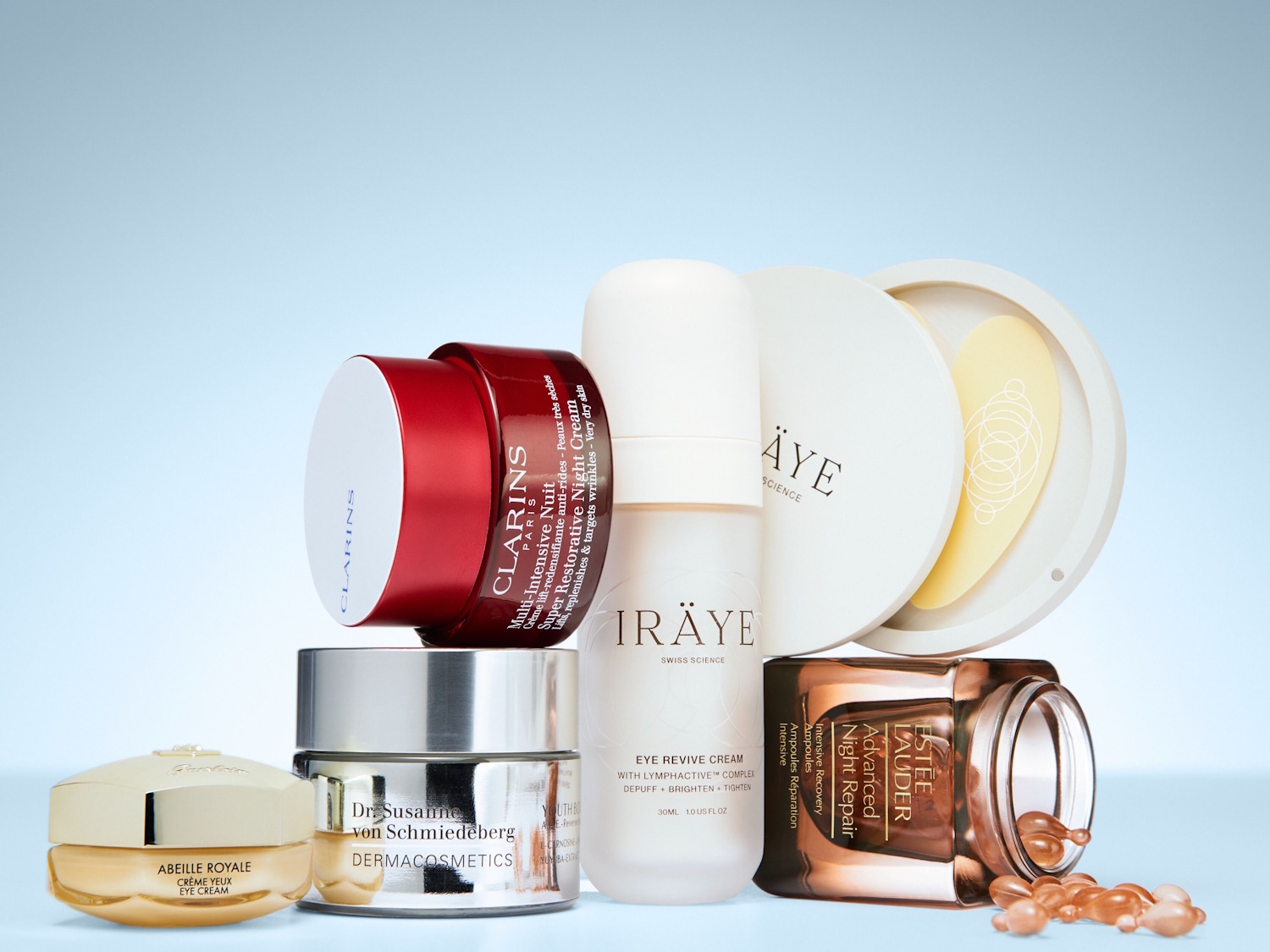 Een verzameling van zes luxe huidverzorgingsproducten, waaronder crèmes en serums, staat op een lichtblauwe achtergrond, klaar om de huid te verjongen en te herstellen.