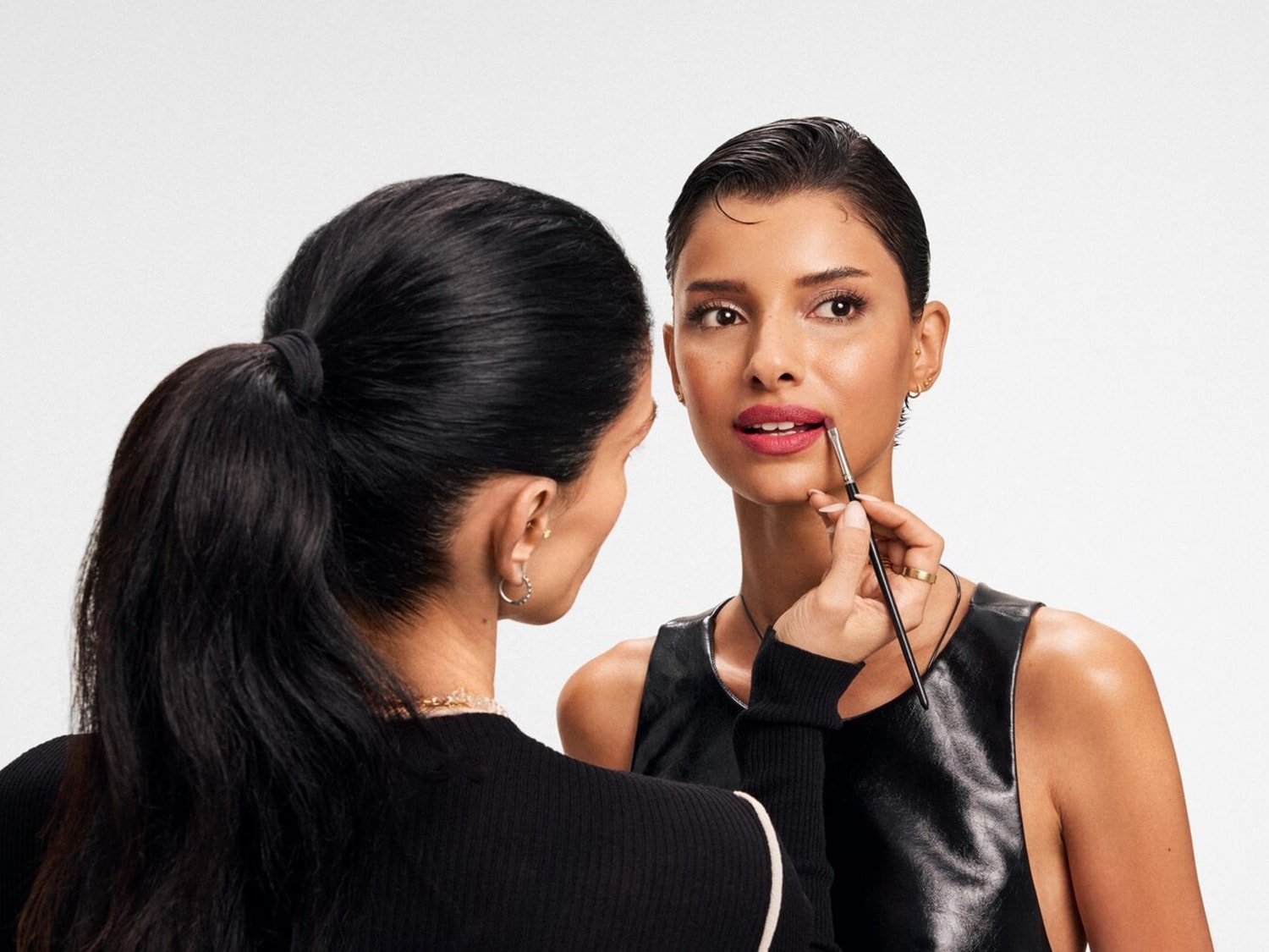 O artistă de machiaj aplică cu grijă ruj roșu-rozaliu pe buzele unui model, folosind o pensulă fină pentru precizie, evidențiind un look sofisticat și elegant.