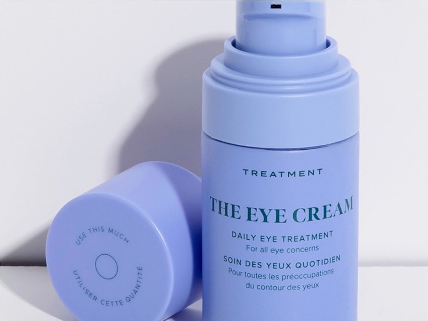 The Eye Cream, a daily eye treatment for all eye concerns, comes in a light purple bottle with a pump dispenser, and its cap suggests the amount to use with the text "USE THIS MUCH" around a small circle.