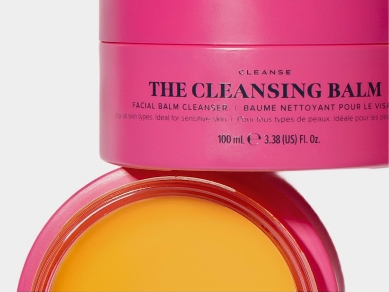 The Cleansing Balm, a facial balm cleanser for all skin types, including sensitive skin, is presented in a vibrant pink jar with a rich yellow balm visible inside, containing 100 mL or 3.38 US Fl. Oz.