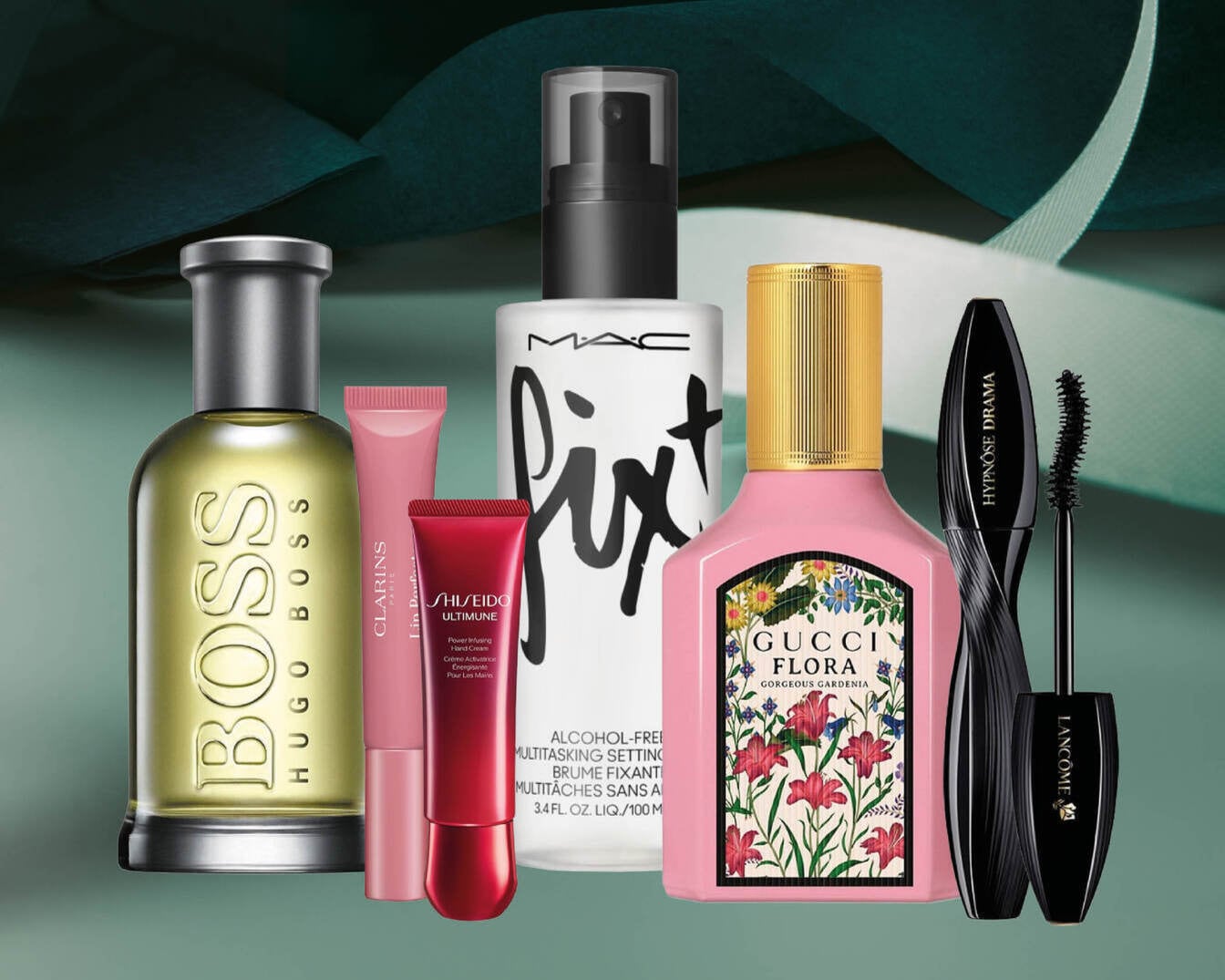 Šiame vaizde matomas "Hugo Boss" kvepalų buteliukas, "Clarins" ir "Shiseido" rankų kremai, "MAC Fix+ Setting Spray", "Gucci Flora Gorgeous Gardenia" kvepalai ir "Lancôme Hypnôse Drama" blakstienų tušas, išdėstyti ant tamsiai žalio fono.