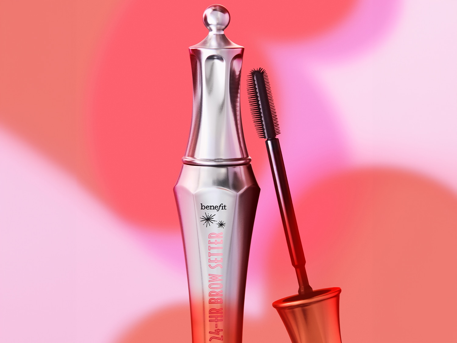 Benefit 24-HR Brow Setter, ein silberner, schlanker Stift mit einem schwarzen Bürstchen, das aus der Kappe ragt, steht auf einem leuchtend roten Hintergrund.