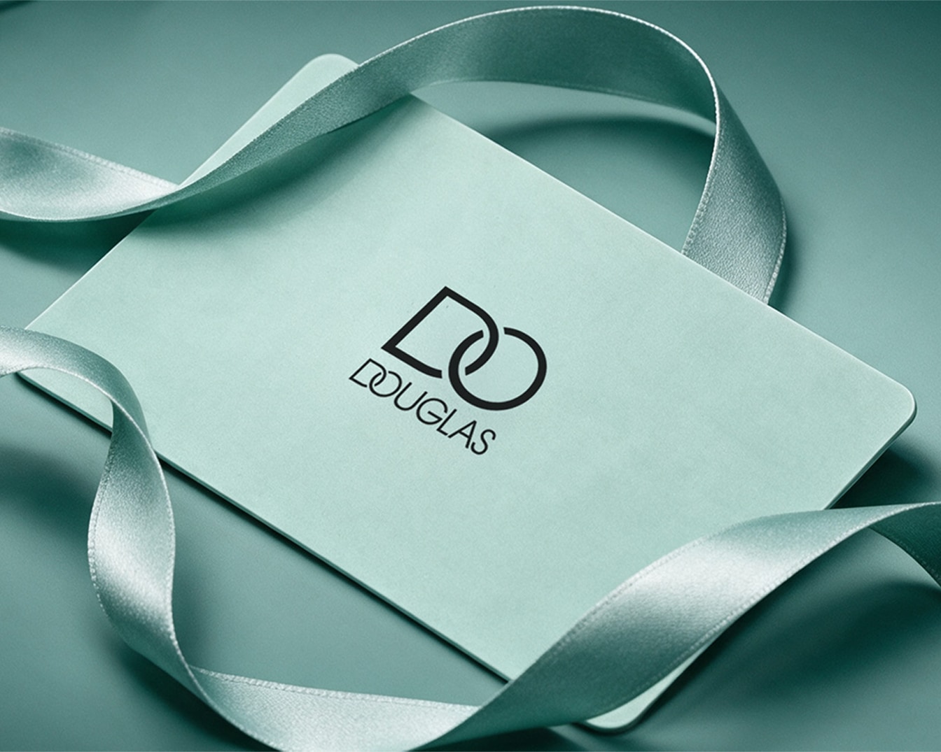 Une carte-cadeau Douglas vert menthe avec le logo Douglas noir est posée sur un fond vert menthe, ornée d'un ruban de satin vert menthe.