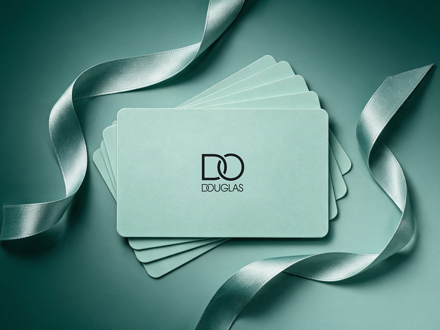 Plusieurs cartes-cadeaux Douglas vert menthe sont disposées en éventail sur un fond vert sarcelle, ornées d'un ruban de soie vert clair qui serpente autour d'elles.