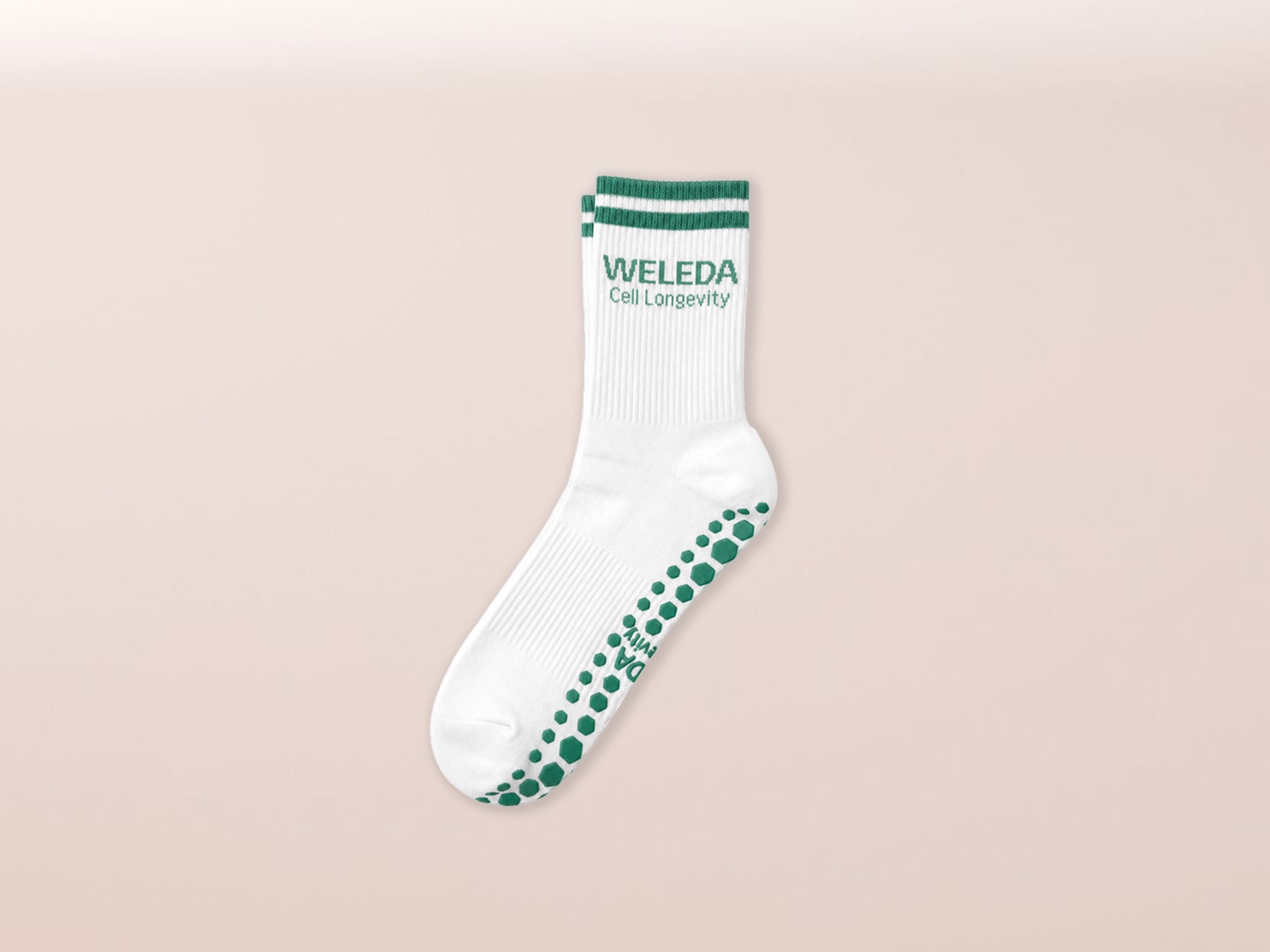 Weiße Socken mit grünen Streifen und dem Weleda-Logo, die auf der Unterseite grüne, sechseckige Anti-Rutsch-Punkte aufweisen.