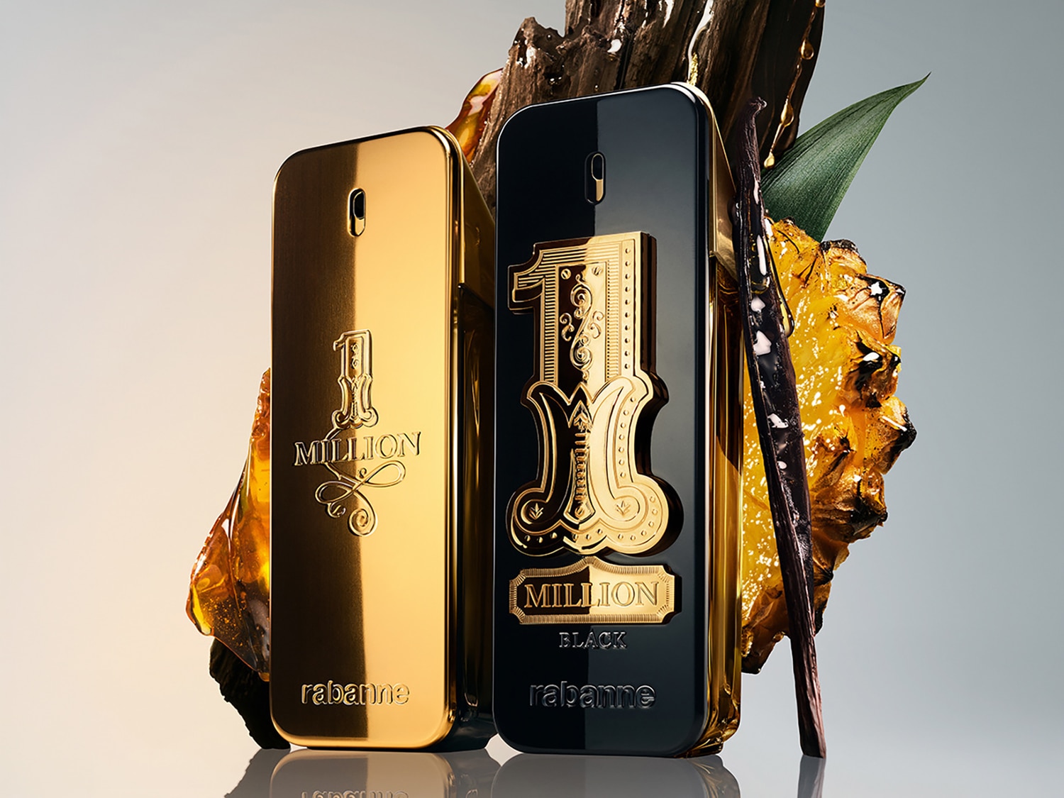Due flaconi di profumo Rabanne 1 Million, uno dorato e uno nero, sono affiancati su uno sfondo grigio chiaro, con elementi naturali come legno, foglie verdi e ananas che aggiungono un tocco esotico.