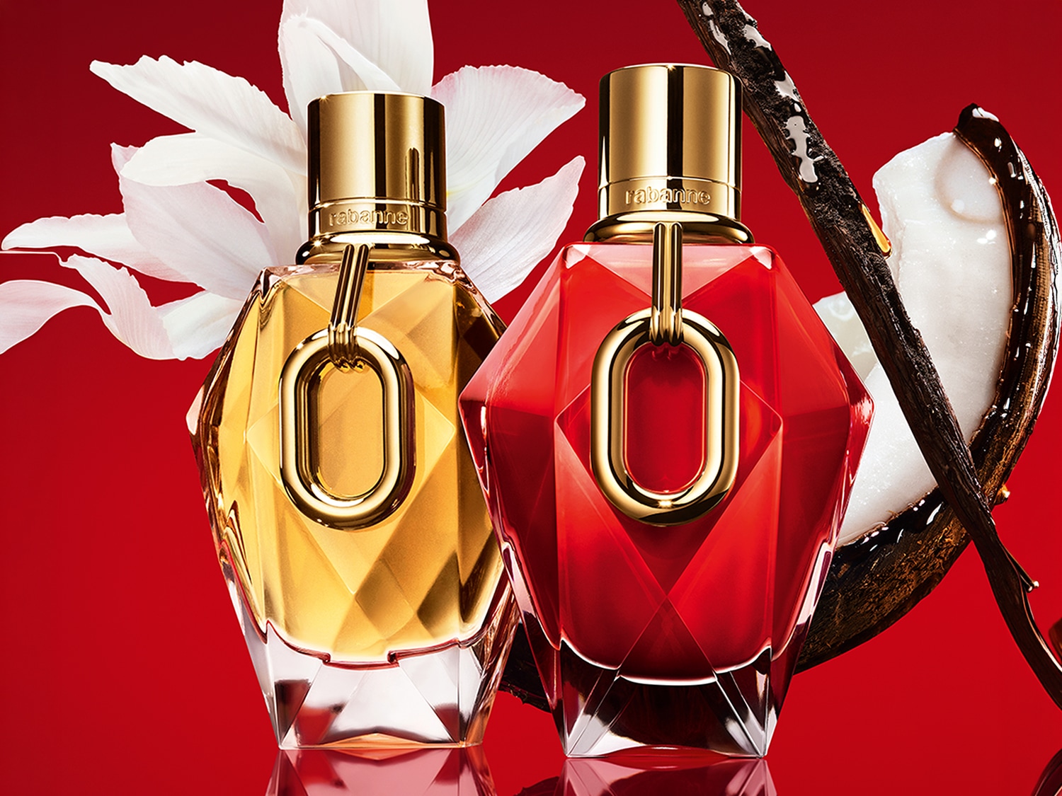 Due flaconi di profumo Rabanne, uno dorato e uno rosso, con tappi dorati e un anello dorato al centro, sono affiancati su uno sfondo rosso, con petali bianchi e baccelli di vaniglia che aggiungono un tocco esotico.