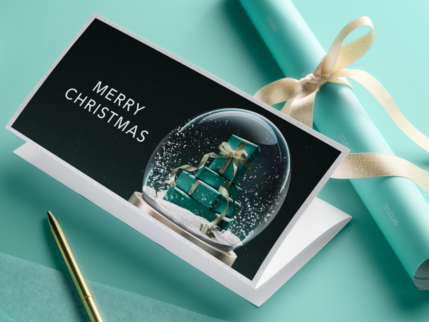 O felicitare de Crăciun cu textul "MERRY CHRISTMAS" și un glob de zăpadă cu cadouri turcoaz, alături de o rolă de hârtie de împachetat Douglas și un pix auriu.
