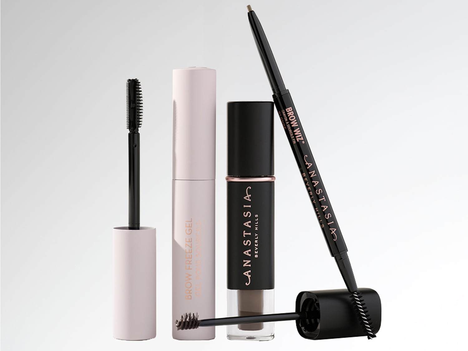 Mehrere Anastasia Beverly Hills Augenbrauenprodukte sind nebeneinander vor einem hellen Hintergrund angeordnet: darunter eine hellrosa Tube Brow Freeze Gel und ein Brow Wiz Augenbrauenstift, dessen Bürste zu sehen ist.
