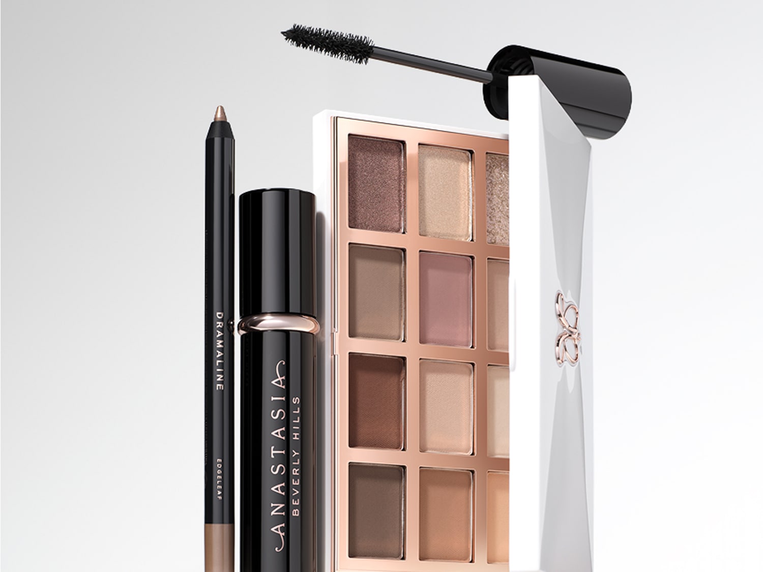 Ein brauner Eyelinerstift, ein schwarzer Mascara und eine geöffnete Lidschattenpalette mit 12 Farbtönen sind auf einem weißen Hintergrund angeordnet.