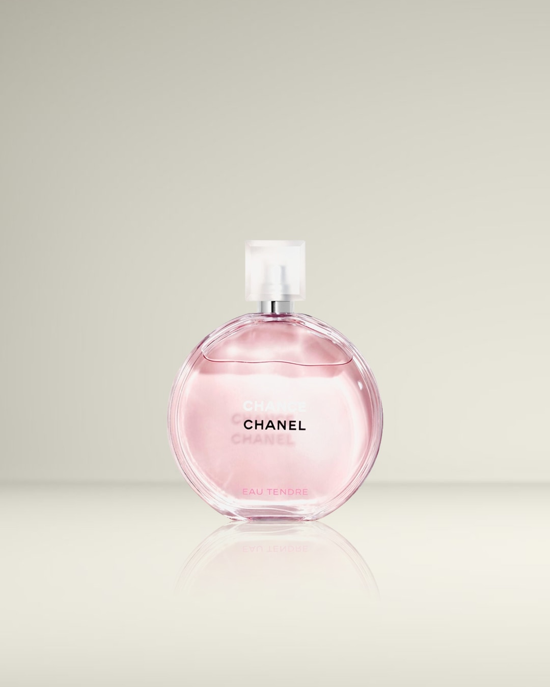 Een ronde, glazen fles van Chanel Chance Eau Tendre parfum met een lichtroze vloeistof en een transparante dop, staat op een glanzend oppervlak.