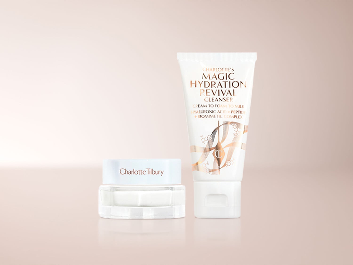 Charlotte Tilbury Magic Hydration Revival Cleanser, eine weiße Tube mit goldener Schrift, steht neben einem Charlotte Tilbury Tiegel mit weißem Deckel und klarem Boden, der eine weiße Creme enthält.