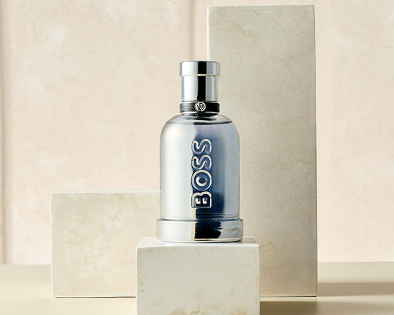 Der BOSS Bottled Marine Eau de Toilette Flakon, gefüllt mit hellblauer Flüssigkeit, steht auf einem hellen Marmorblock, umgeben von weiteren Marmorstücken vor einem cremefarbenen Hintergrund.