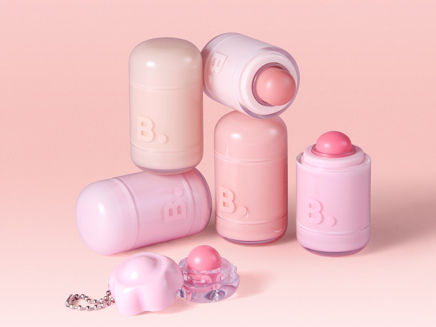 Découvrez une collection de baumes à lèvres B. en forme de pilule, dans des tons de rose et de beige, avec un porte-clés assorti, parfaits pour des lèvres hydratées et colorées.