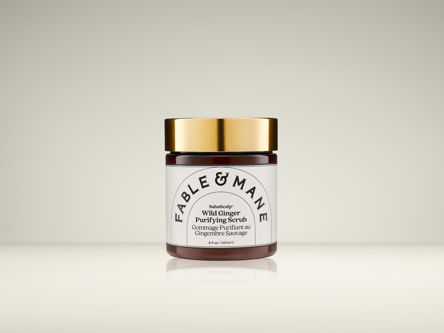 De Fable & Mane SahaScalp Wild Ginger Purifying Scrub in een donkerbruine pot met gouden deksel, met een wit etiket met zwarte tekst, staat centraal op een lichte achtergrond.