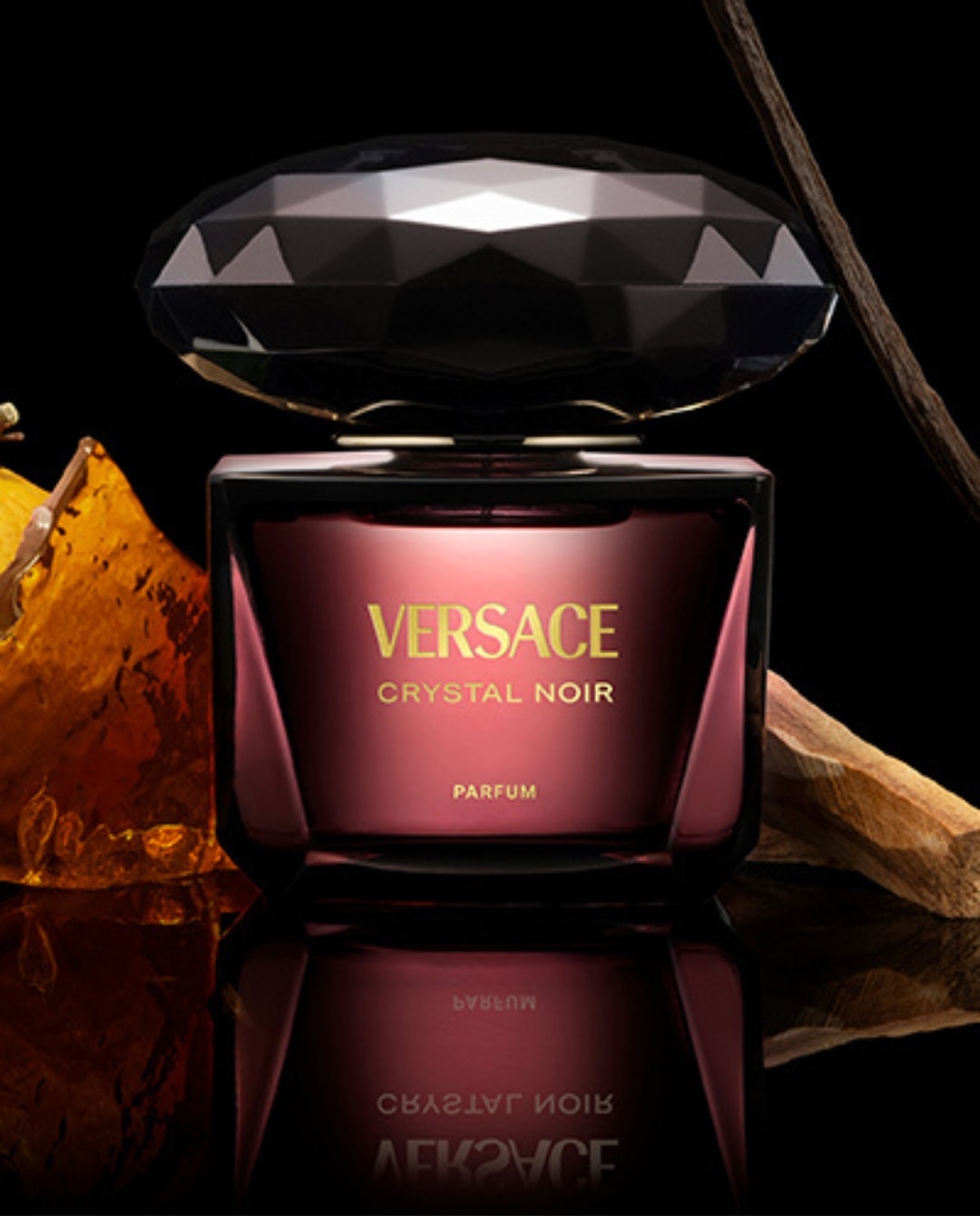 Le parfum Versace Crystal Noir est présenté dans un flacon en verre teinté de rouge foncé avec un bouchon noir à facettes, reflétant son élégance et son mystère.