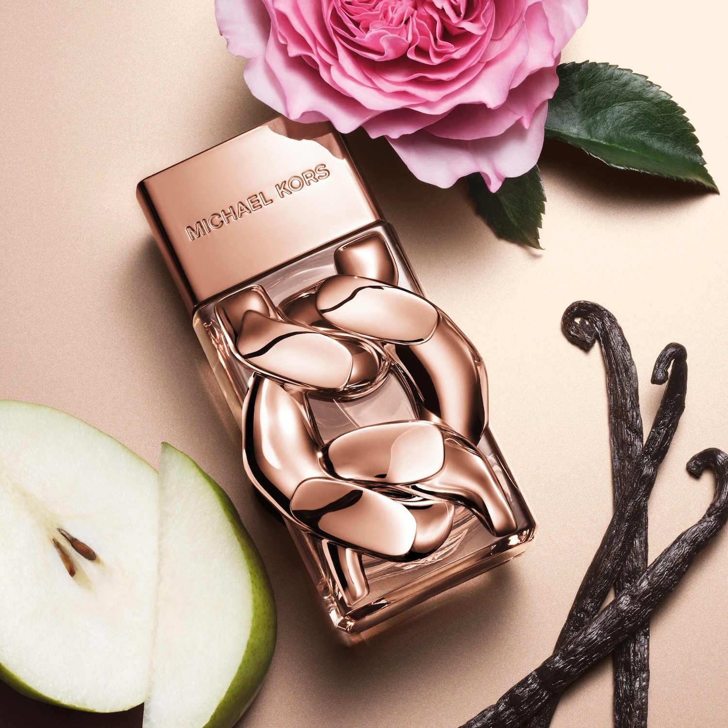 Le parfum Michael Kors est présenté dans un flacon rectangulaire en verre transparent avec un bouchon et des ornements en forme de chaîne couleur or rose, posé sur un fond doré, accompagné d'une rose rose, de gousses de vanille et d'une poire coupée.