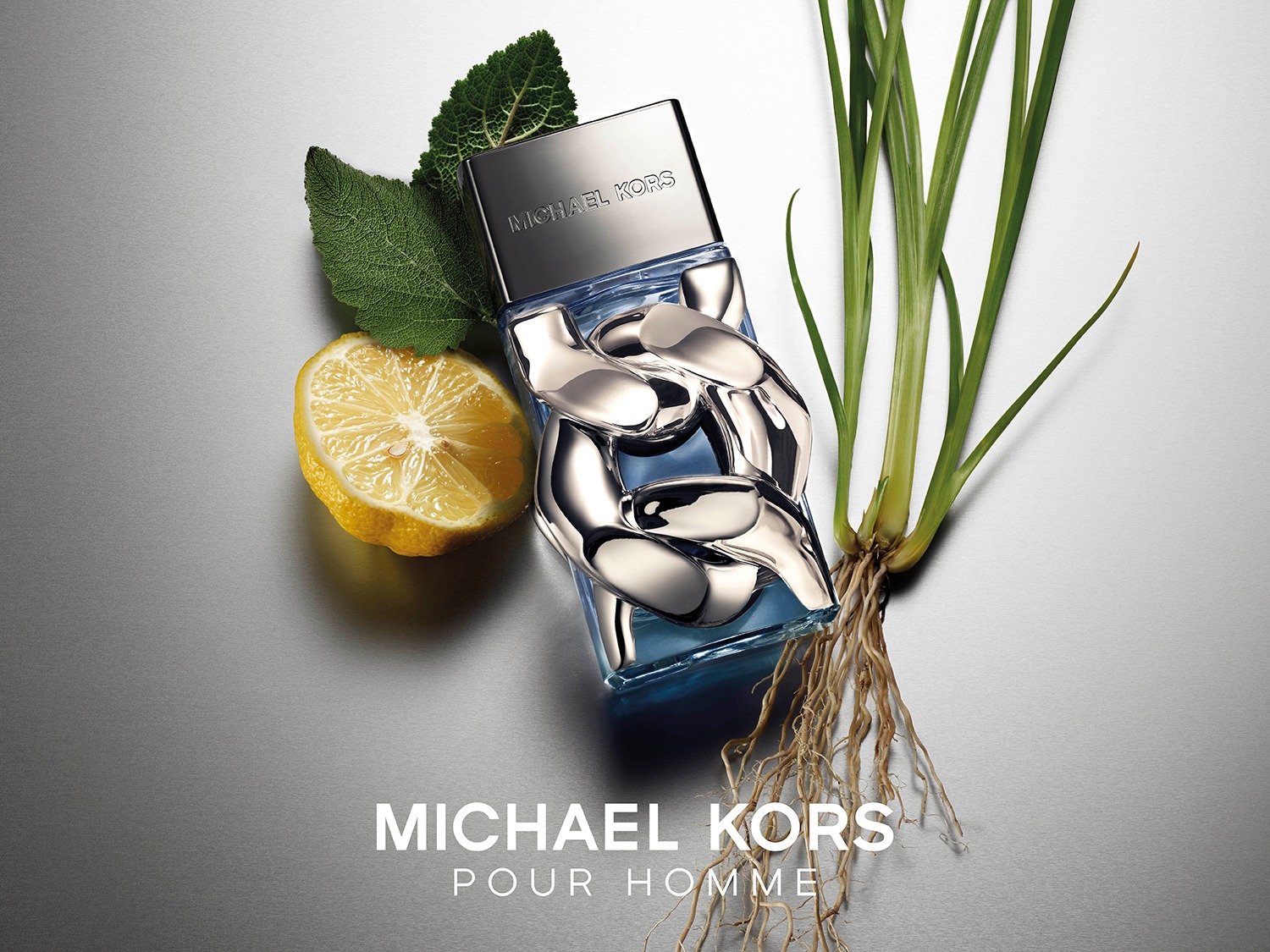 Le parfum Michael Kors Pour Homme est présenté dans un flacon bleu avec des maillons de chaîne argentés, accompagné d'un citron coupé, de feuilles vertes et d'une plante à racines, sur un fond gris métallique.