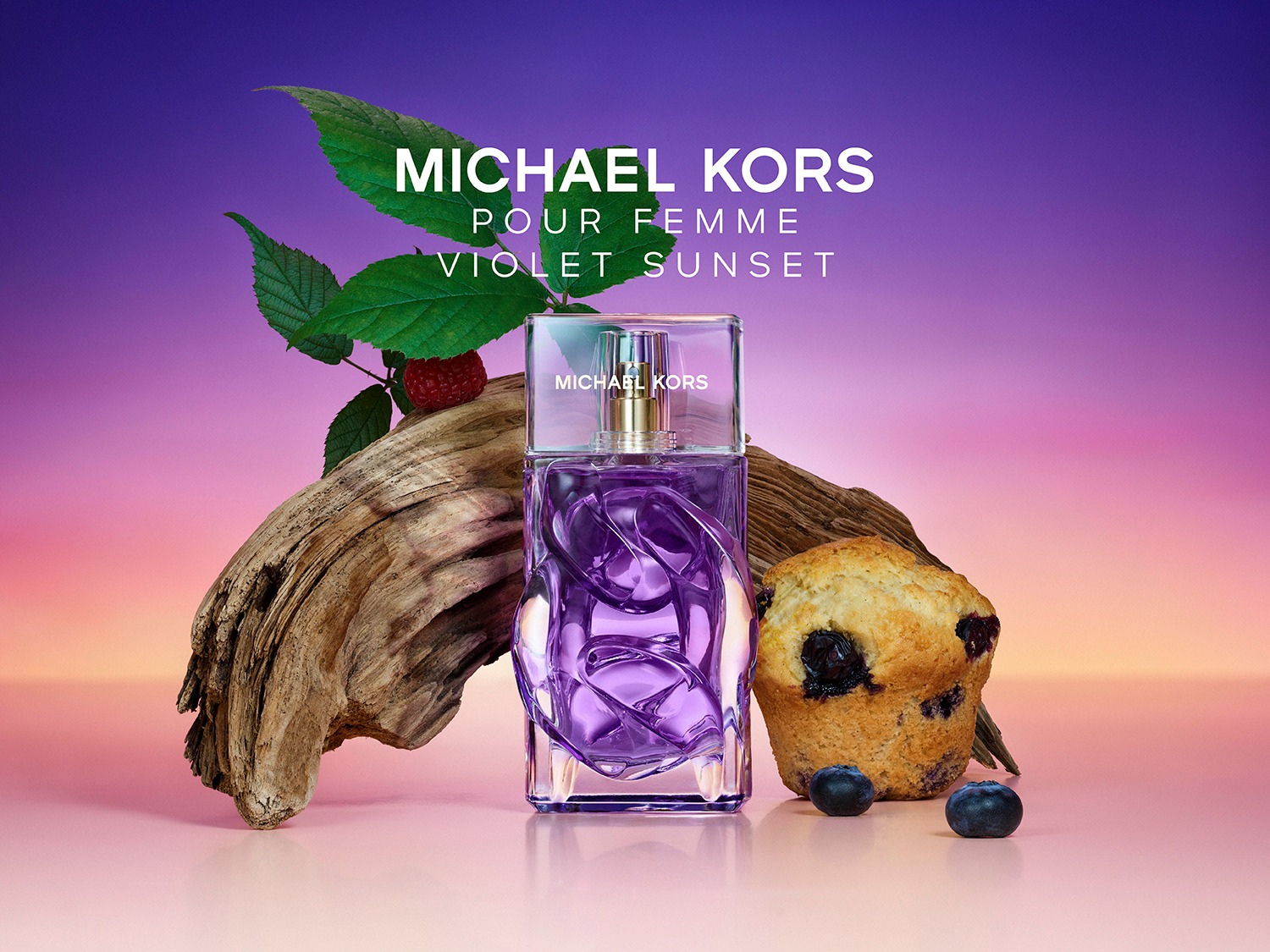 Le parfum Michael Kors Pour Femme Violet Sunset est présenté dans une bouteille en verre violette avec un bouchon transparent, posée sur un morceau de bois flotté, accompagnée d'une feuille verte, d'une framboise, d'un muffin aux myrtilles et de deux myrtilles, le tout sur un fond dégradé de violet et d'orange.